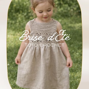Op de afbeelding: Een jong meisje draagt een beige gehaakte top en een bijpassende linnen jurk. De tekst "Brise d'Été Tuto Crochet" is zichtbaar. De jurk heeft een ronde halslijn en een gerimpelde rok. De achtergrond is vaag groen.