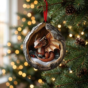 May include: A round, hollowed-out tree trunk ornament featuring a small, orange-scaled dragon with wings inside. The ornament has a red ribbon for hanging and the name William is inscribed in gold script at the bottom of the textured bark frame.