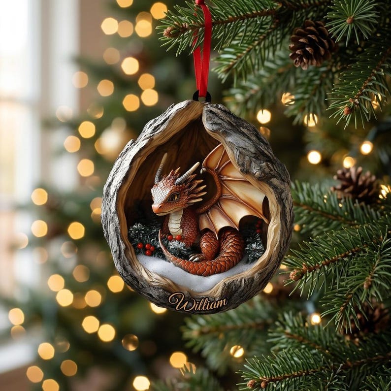 May include: A round, hollowed-out tree trunk ornament featuring a small, orange-scaled dragon with wings inside. The ornament has a red ribbon for hanging and the name William is inscribed in gold script at the bottom of the textured bark frame.