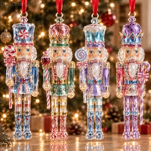 Puede incluir: Cuatro adornos decorativos de cascanueces hechos de vidrio facetado multicolor. Cada figura lleva un sombrero alto y ornamentado y sostiene un bastón con temática de dulces. Los cascanueces presentan patrones geométricos complejos en tonos azules, rosas y morados, suspendidos por cintas rojas.