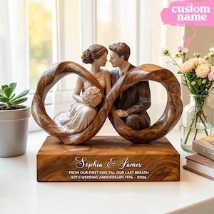 May include: A wooden wedding anniversary sculpture featuring a couple within an infinity symbol. The base is engraved with "Sophia & James" and anniversary details. The sculpture includes a bride holding a bouquet and a groom in a suit. The text on the image says "custom name".