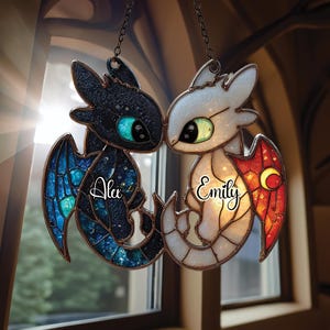 以下が含まれることがあります： チェーンで吊るされた、黒と白のステンドグラスのドラゴンオーナメント2つ。黒いドラゴンは青い翼と「Alex」という名前を持っています。白いドラゴンは赤い翼と「Emily」という名前を持っています。