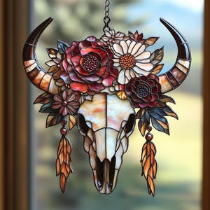 May include: A stained glass bull skull with large curved horns and a floral crown. The skull is cream and brown, with red, white, and brown flowers. Two orange and brown feather pendants hang below the skull. The horns are brown and tan.
