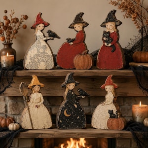 May include: Six decorative wooden witch figurines arranged on a shelf. Each figure wears a pointed hat and a dress with distinct patterns or solid colours, featuring motifs like black cats, crows, pumpkins, stars, and a crescent moon.