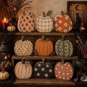 May include: A collection of nine decorative wooden pumpkins arranged on a three-tiered shelf. Each pumpkin features a unique hand-painted design, including leopard print, black plaid, white flowers, polka dots, solid orange, vines, stripes, and hearts.