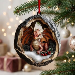 May include: A round, hollowed-out tree trunk ornament featuring a small, orange-scaled dragon with wings, sitting on a patch of white snow with green holly leaves and red berries. The name William is inscribed in white script at the bottom.