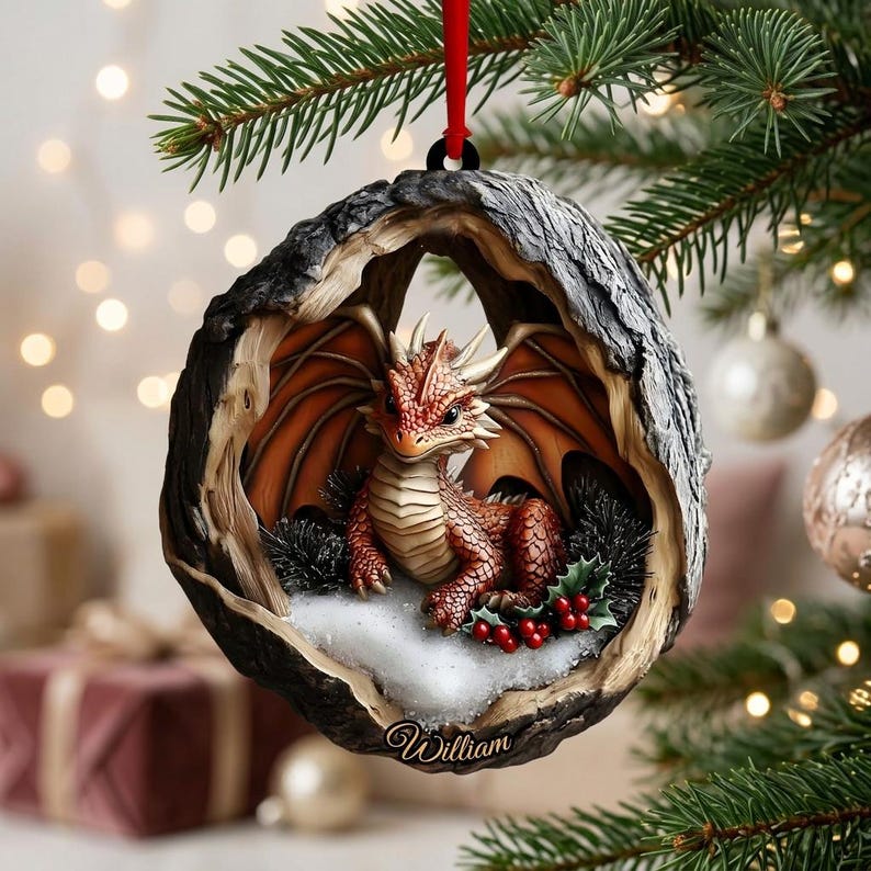 May include: A round, hollowed-out tree trunk ornament featuring a small, orange-scaled dragon with wings, sitting on a patch of white snow with green holly leaves and red berries. The name William is inscribed in white script at the bottom.