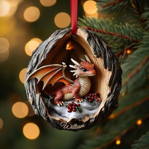 May include: A round Christmas ornament shaped like a hollowed-out tree trunk featuring a small orange dragon with wings inside. The dragon sits on a snowy base with red holly berries. The name William is printed in white script at the bottom.