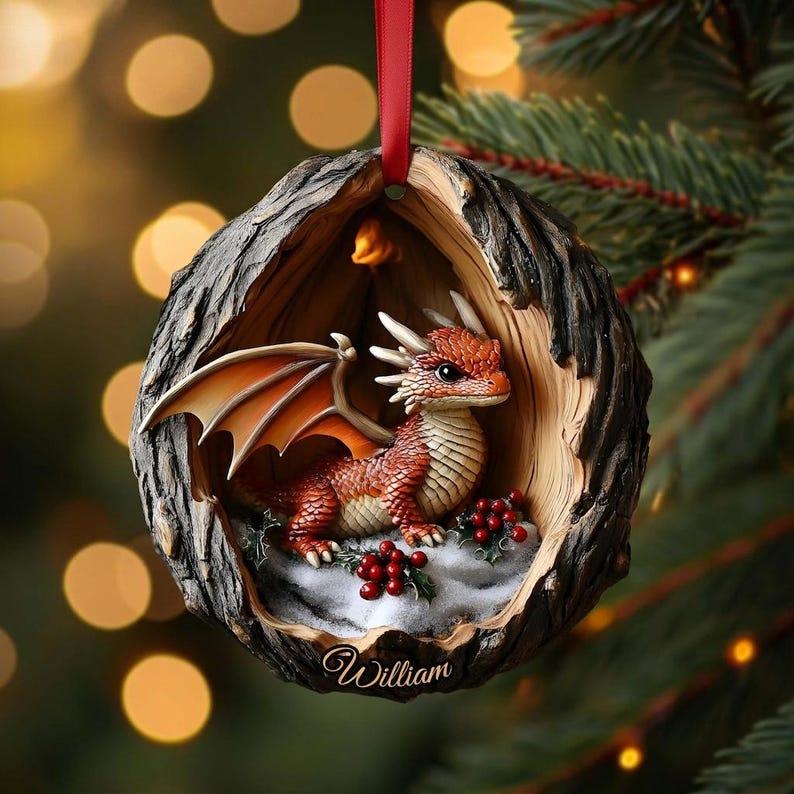May include: A round Christmas ornament shaped like a hollowed-out tree trunk featuring a small orange dragon with wings inside. The dragon sits on a snowy base with red holly berries. The name William is printed in white script at the bottom.