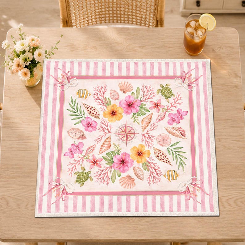 May include: Square placemat with a coastal theme. The design features pink and white stripes around the border, framing a central pattern of seashells, flowers, coral, and a compass rose. The color palette includes pink, yellow, green, and beige.