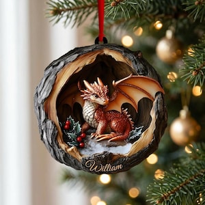 May include: A round, tree-hollow shaped Christmas ornament featuring a small, orange-scaled dragon with wings, sitting near green holly leaves and red berries. The base of the ornament is inscribed with the name William in cursive script.