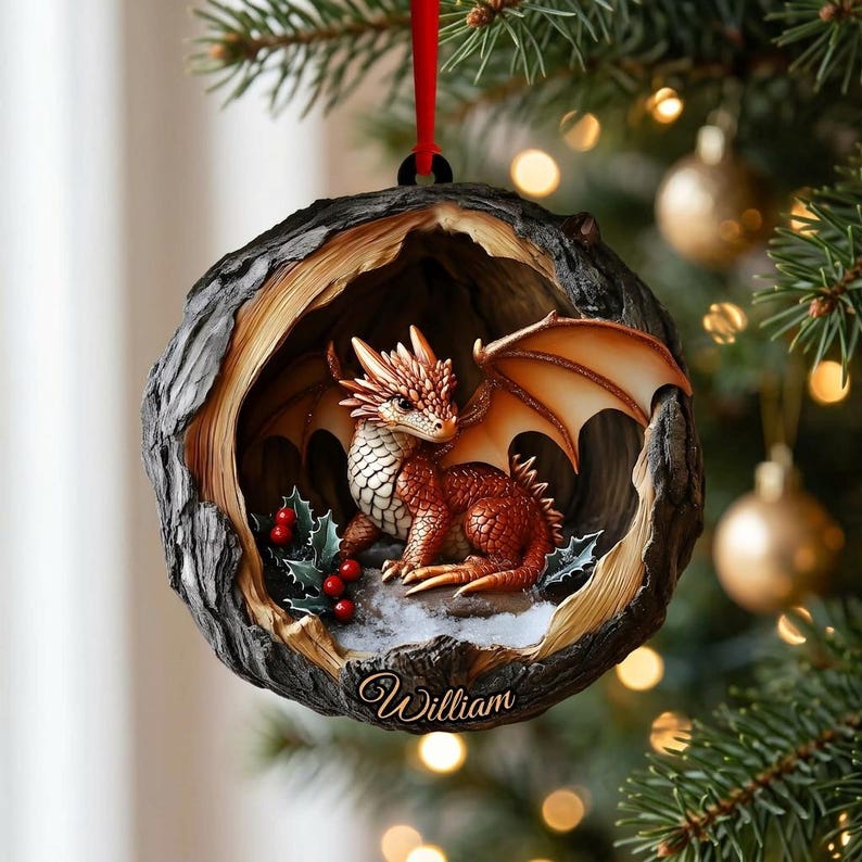 May include: A round, tree-hollow shaped Christmas ornament featuring a small, orange-scaled dragon with wings, sitting near green holly leaves and red berries. The base of the ornament is inscribed with the name William in cursive script.