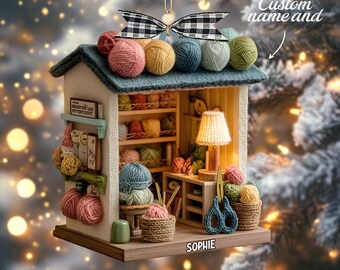 May include: A miniature craft room ornament featuring a teal roof topped with colorful yarn balls and a black and white gingham bow. The interior displays shelves of yarn, a small lamp, and scissors. The base is personalized with the name SOPHIE.