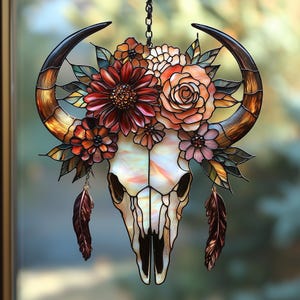 May include: Stained glass bull skull with flowers and feathers. The skull is white and cream with black outlines. The horns are brown and gold. The flowers are red, orange, and pink. Two brown feathers hang below.