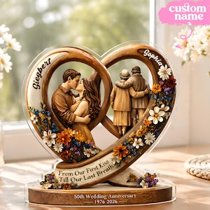 Puede incluir: Una escultura de aniversario en forma de corazón con dos corazones entrelazados. Uno muestra a una pareja besándose, el otro a una pareja mayor abrazándose. La base dice "From Our First Kiss Till Our Last Breath" y "50th Wedding Anniversary 1976-2026".