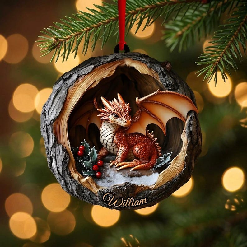 May include: A round, hollowed-out tree trunk ornament featuring a small, orange-scaled dragon with wings inside. The dragon sits near green holly leaves and red berries. The name William is inscribed in white script at the bottom of the wood.