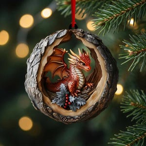 May include: A round, wood-textured Christmas ornament featuring a detailed red dragon with cream-colored horns and wings. The dragon sits amidst green holly leaves and red berries. The name William is inscribed in cursive at the bottom of the ornament.