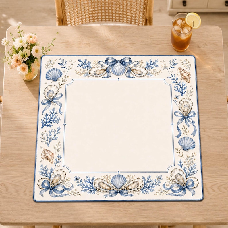 Puede incluir: Un mantel individual cuadrado con un centro blanco y un borde decorativo con ilustraciones azules de conchas marinas, ostras con perlas, ramas de coral y cintas atadas. El dise&ntilde;o es sim&eacute;trico y enmarca el cuadrado blanco liso del centro.