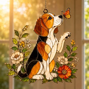 Könnte beinhalten: Ein Buntglas-Suncatcher mit einem Beagle-Hund aus braunen, schwarzen und weißen Segmenten. Der Hund schaut zu einem orangefarbenen Schmetterling auf, der auf seiner Nase sitzt. Das Design ist von grünen Blättern sowie weißen und orangefarbenen Blumen umgeben.