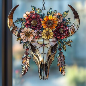 May include: Stained glass bull skull with a floral crown. The skull is cream-colored with brown accents, and the horns are a mix of brown and cream. The floral crown features red, orange, and yellow flowers with green leaves. Two decorative feathers hang below.