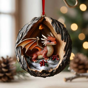 May include: A round, hollowed-out tree bark ornament featuring a small, orange-scaled dragon with wings inside. The dragon sits on a snowy base decorated with red holly berries. The name William is inscribed in cursive script at the bottom edge.