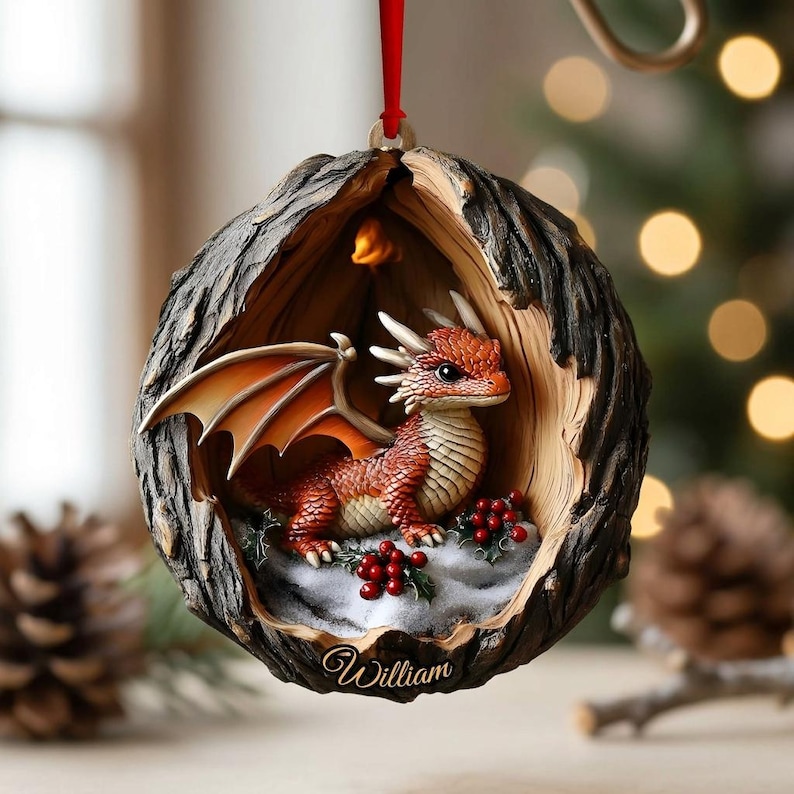 May include: A round, hollowed-out tree bark ornament featuring a small, orange-scaled dragon with wings inside. The dragon sits on a snowy base decorated with red holly berries. The name William is inscribed in cursive script at the bottom edge.