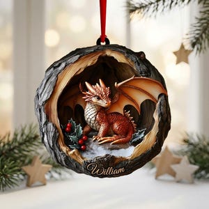 May include: A round, hollowed-out tree trunk ornament featuring a small, orange-scaled dragon with wings inside. The dragon sits near green holly leaves and red berries. The base of the ornament is inscribed with the name William in cursive script.
