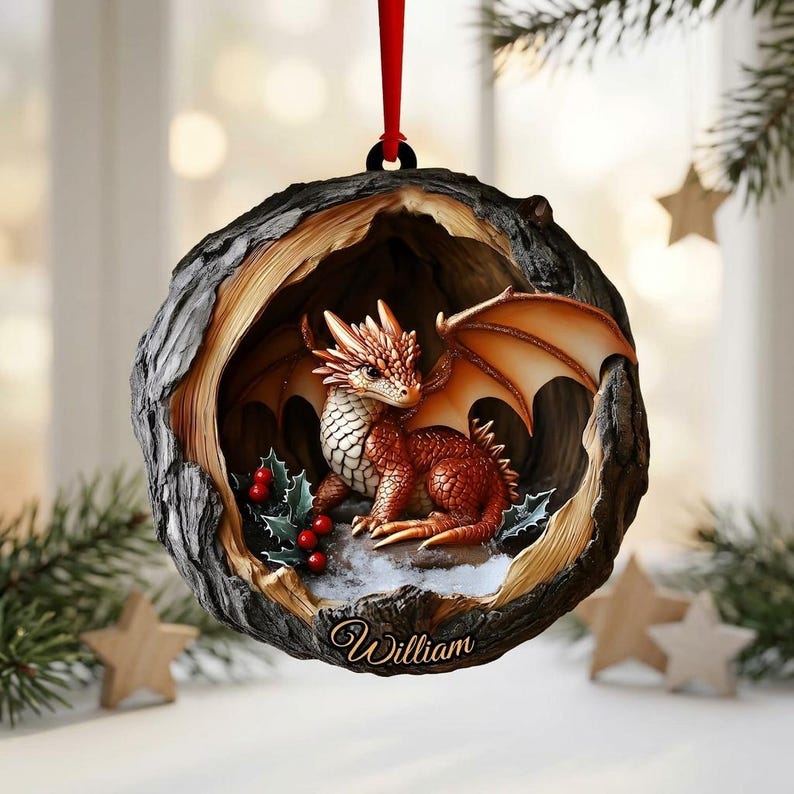 May include: A round, hollowed-out tree trunk ornament featuring a small, orange-scaled dragon with wings inside. The dragon sits near green holly leaves and red berries. The base of the ornament is inscribed with the name William in cursive script.