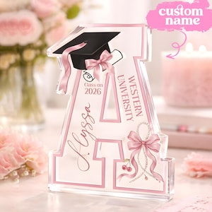 May include: A clear acrylic letter 'A' with pink detailing, a graduation cap, and a pink bow. The letter features the text 'Western University', 'Class on 2026', and the name 'Alyssa'. A pink bow and cherries are also featured.