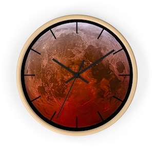 Peut inclure: Une horloge murale ronde avec un cadre en bois clair. Le cadran présente un dégradé rouge et orange rappelant une planète. Les aiguilles et les index noirs complètent le design.