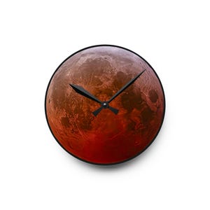 Puede incluir: Un reloj de pared redondo con una imagen roja y naranja de Marte. El reloj tiene agujas negras.