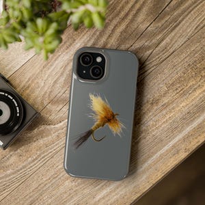 May include: A gray phone case with a realistic image of a brown and yellow fly fishing lure.