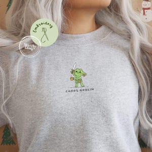 May include: A grey sweatshirt with an embroidered green goblin holding a sword and a mug. The text "CHAOS GOBLIN" is embroidered below the goblin. The sweatshirt has a crew neck.