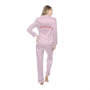 May include: A pink satin pajama set with long sleeves and pants. The back of the top has the text "Sugar Plum Fairy" in a pink and red font.