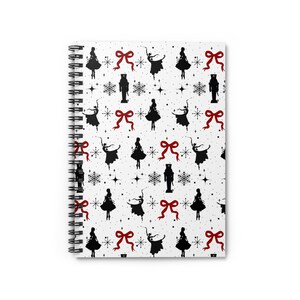 Puede incluir: Una libreta espiral blanca con un patrón negro y rojo. El patrón presenta siluetas de bailarinas, cascanueces, copos de nieve y lazos.