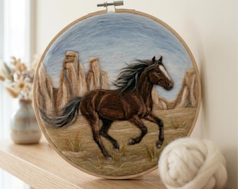 Può includere: Un telaio da ricamo circolare contenente una scena in lana infeltrita di un cavallo marrone con una macchia bianca che corre attraverso un paesaggio desertico con formazioni rocciose color sabbia sotto un cielo azzurro, incorniciato in legno.