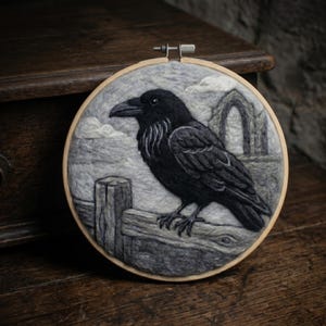 May include: A circular wooden embroidery hoop containing a needle-felted scene of a black raven perched on a wooden fence. The background features a grey sky with white clouds and a stone archway structure, all rendered in textured wool fibers.