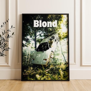 Könnte beinhalten: Gerahmter Kunstdruck mit einem weißen Sportwagen, der in einer Waldszene schwebt. Das Wort "Blond" steht in großen, weißen Buchstaben oben. Das Auto ist nach oben geneigt, mit einem Hintergrund aus Bäumen und Blättern.