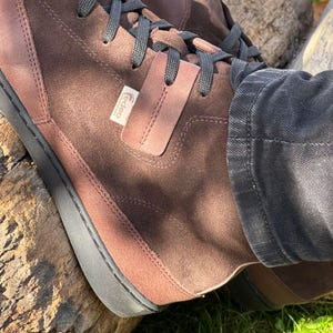 May include: Brown suede high-top sneakers with black laces and a black rubber sole. The brand name "Gadeo" is visible on the side of the shoe.
