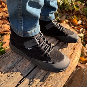 Pu&ograve; includere: Scarpe alte in pelle scamosciata nera con suola in gomma nera e un cinturino grigio con la scritta "Vibram" su di esso.