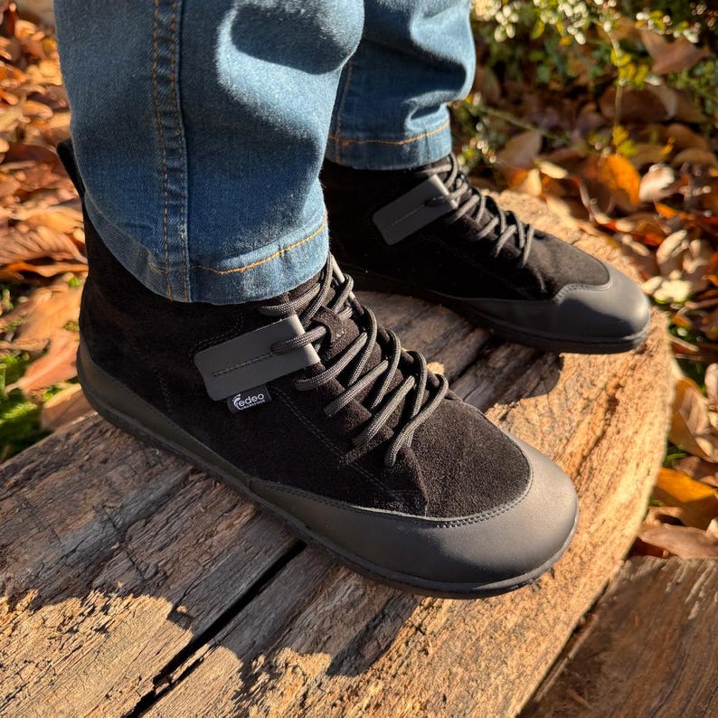 Pu&ograve; includere: Scarpe alte in pelle scamosciata nera con suola in gomma nera e un cinturino grigio con la scritta "Vibram" su di esso.