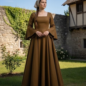 以下が含まれることがあります： 四角いネックラインとフレア袖が特徴の、茶色のロング丈の中世風ドレス。 ドレスは、フィットした胴体とフルスカートが特徴です。 頭飾りも着用しています。 ドレスは無地のテクスチャード加工された生地で作られています。 背景には石壁と緑があります。