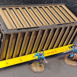 Może przedstawiać: Drewniany model kontenera transportowego z czarną obw&oacute;dką. Kontener ma około 30 cm długości i 10 cm szerokości. Kontener stoi na stole z ż&oacute;łtą miarką.