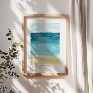 May include: Watercolor print of a beach scene in a wooden frame. The artwork features a blue ocean, a yellow beach, and a light blue sky. The words "made waves" are written in a small, cursive font at the bottom of the print.