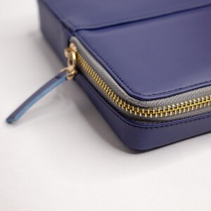 May include: A close-up of a dark blue leather zippered pouch with a gold zipper. The zipper pull is blue.