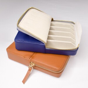 May include: A blue leather jewelry box with a zipper closure and a beige interior. The box is stacked on top of a brown leather jewelry box with a zipper closure.
