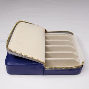 May include: A blue leather zippered case with a soft beige interior and multiple slots for storing jewelry.