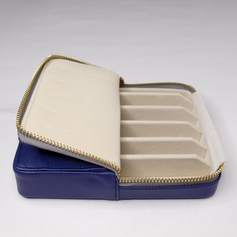 May include: A blue leather zippered case with a soft beige interior and multiple slots for storing jewelry.