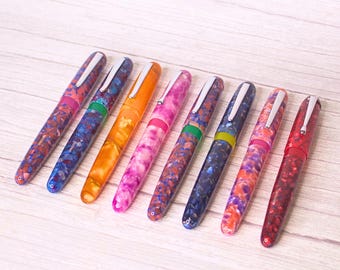 May include: A set of ten colorful fountain pens with marbled patterns. The pens have silver accents and are arranged in a row on a light wood surface.