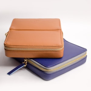 May include: Two zippered leather pouches, one brown and one blue, stacked on top of each other. The brown pouch has a gold zipper and the blue pouch has a silver zipper.